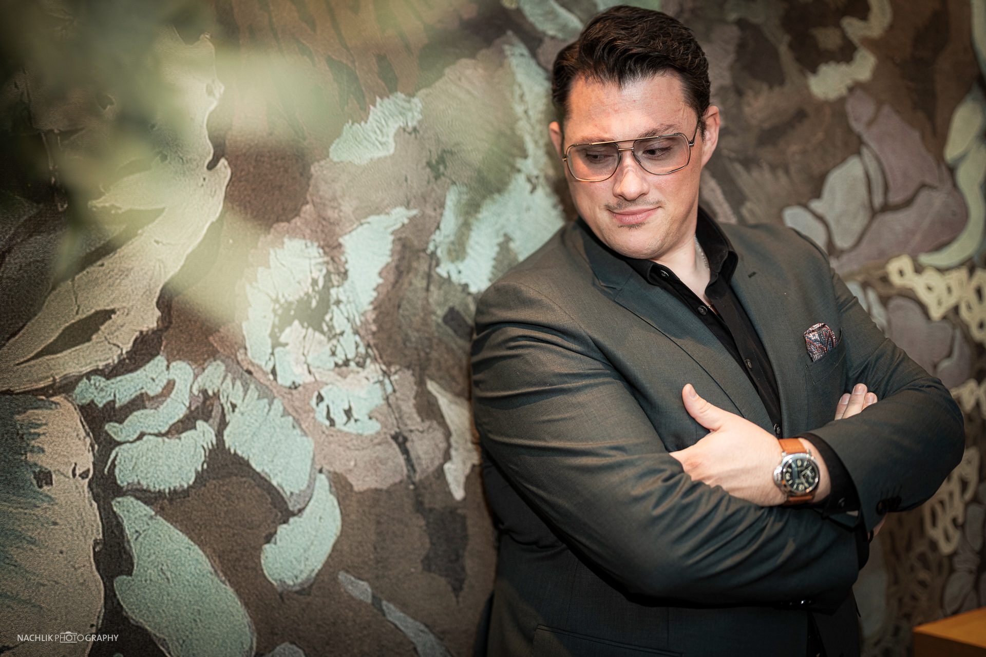 Ricardo Marinello im dunklen Anzug mit verschränkten Armen vor gemusterter Wand