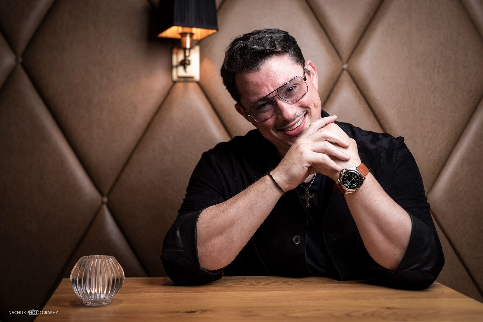 Ricardo Marinello mit gefalteten Händen lächelnd auf der Lederbank
