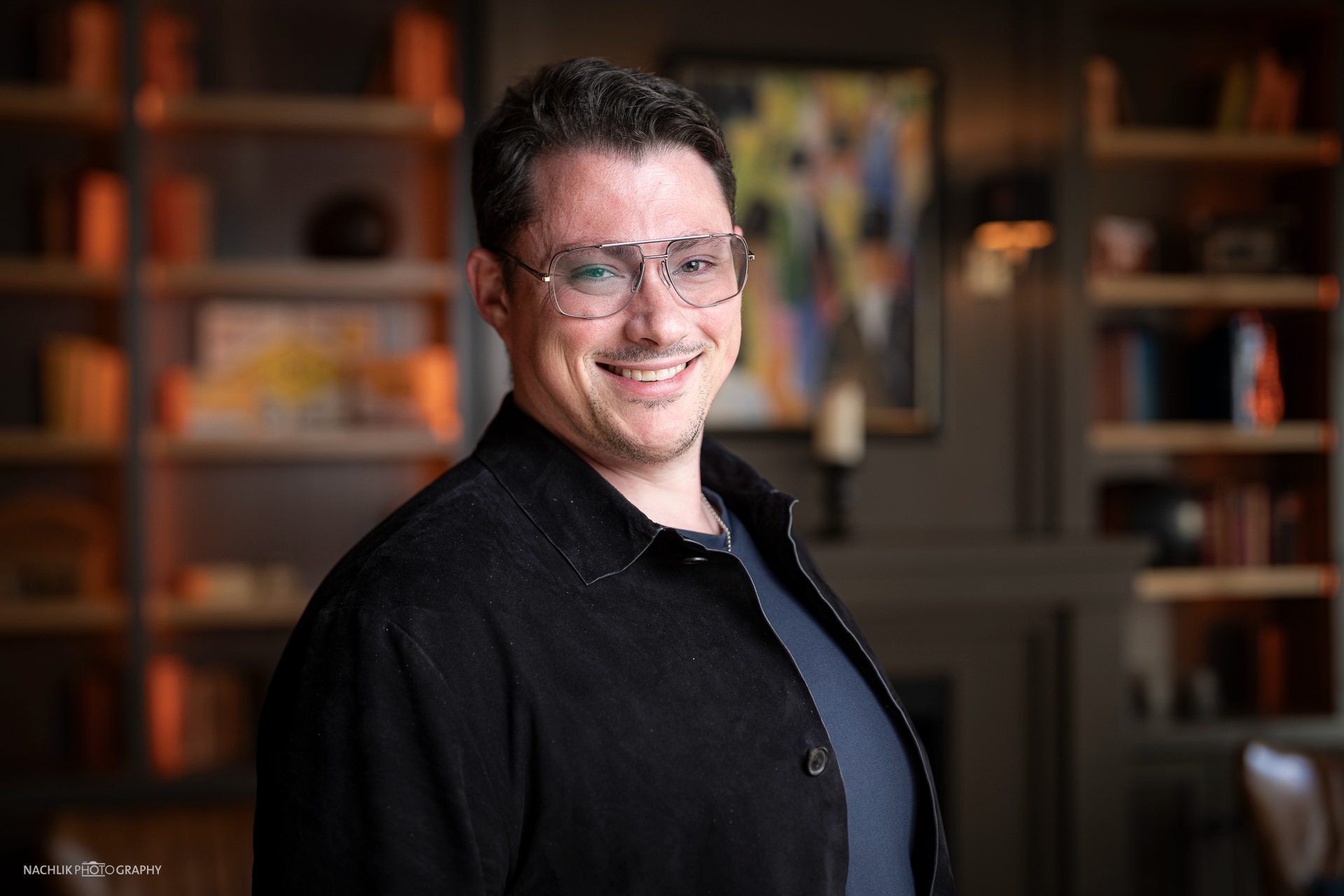Ricardo Marinello stehend vor einer Bücherwand in warm beleuchteter Lounge