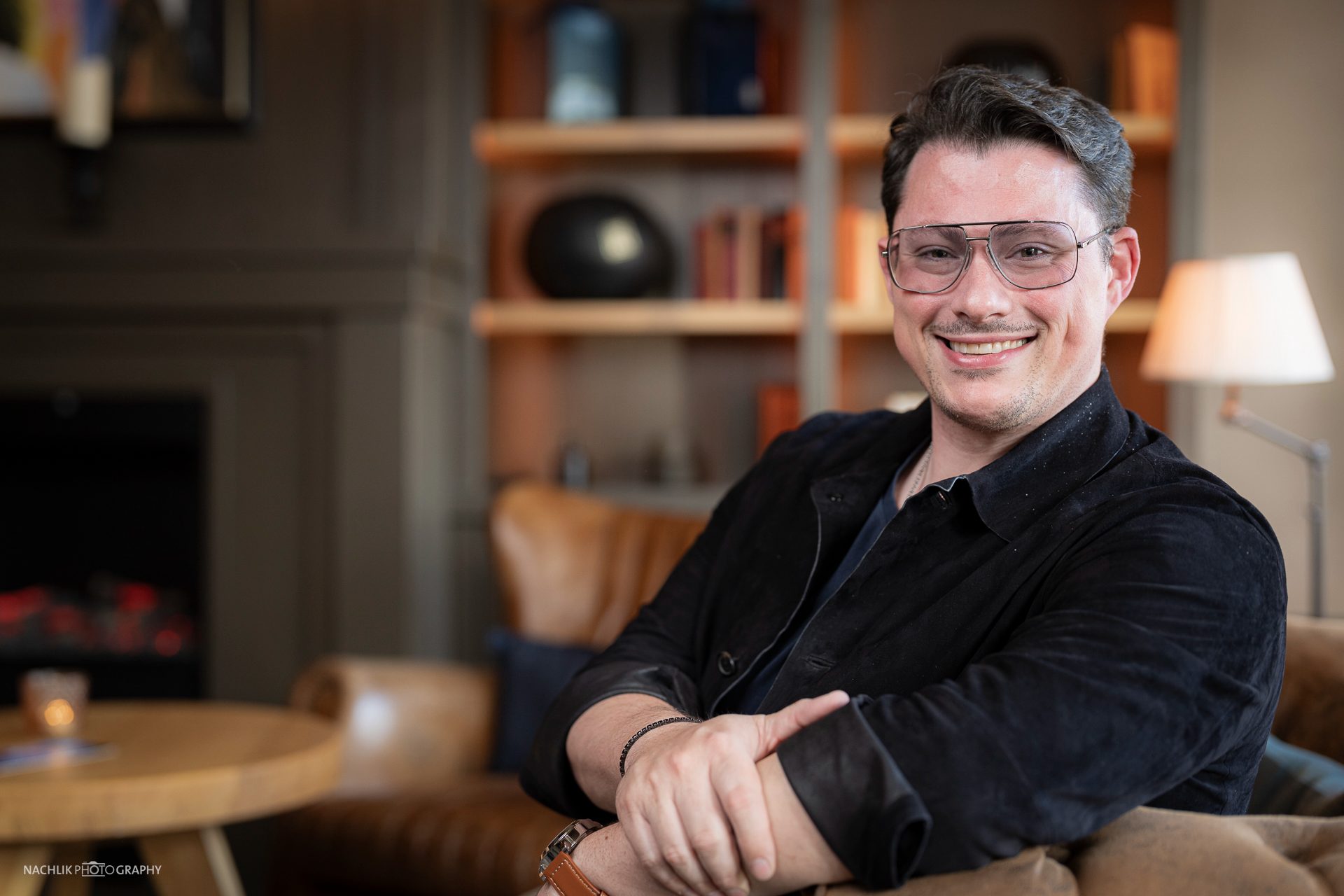 Ricardo Marinello lächelnd im Sessel vor Bücherregal und Stehlampe